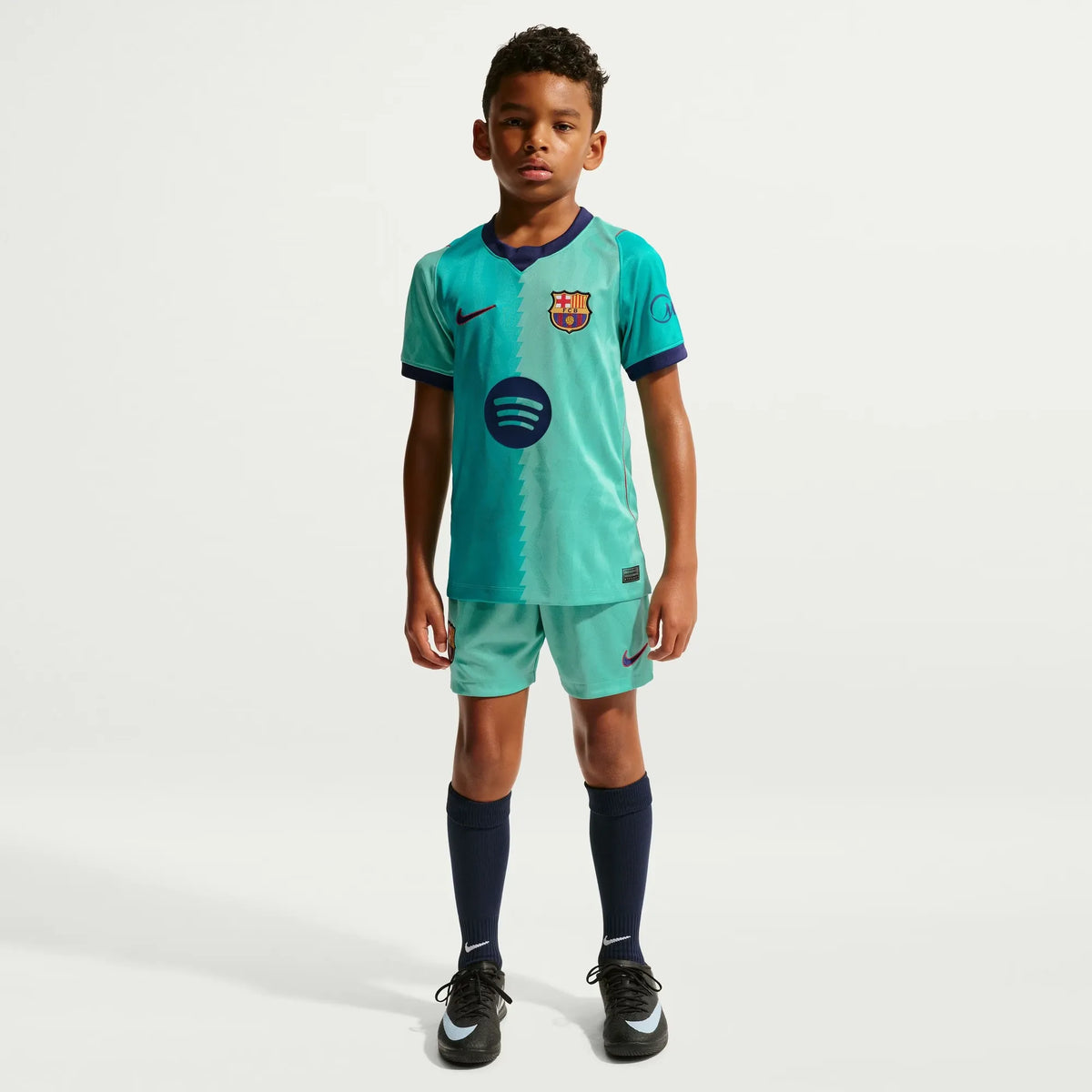 A young boy modeling a Barcelona 2026-2027 third turquoise stadium replica football shirt