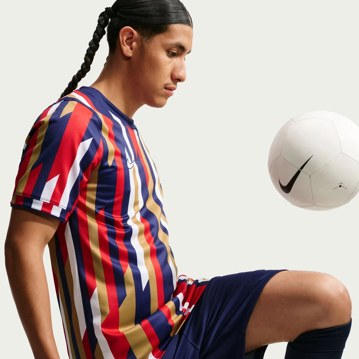 A man wearing aChivas 2026-2027 home white Dri-FIT pre-match top, posed next to a white soccer ball against a light gray background.