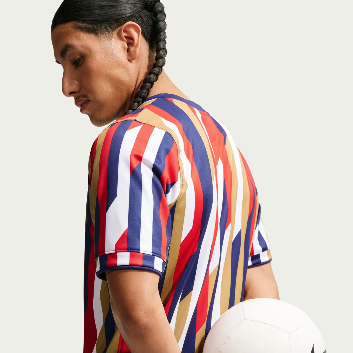A man wearing a Chivas 2026-2027 home white Dri-FIT pre-match top, holding a white soccer ball against a light gray background.