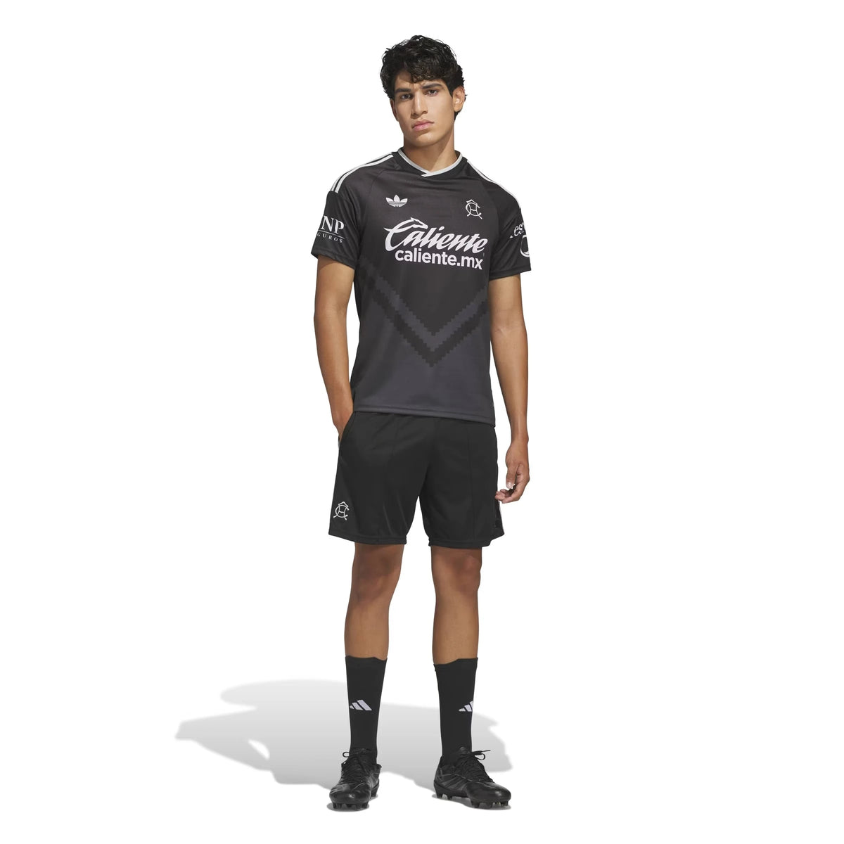 A male model wearing aClub America 2026-2027 away black replica football shirt, featuring a short-sleeve jersey with white sponsor logos and Adidas logo, paired with black shorts, socks, and cleats, on a white studio background.