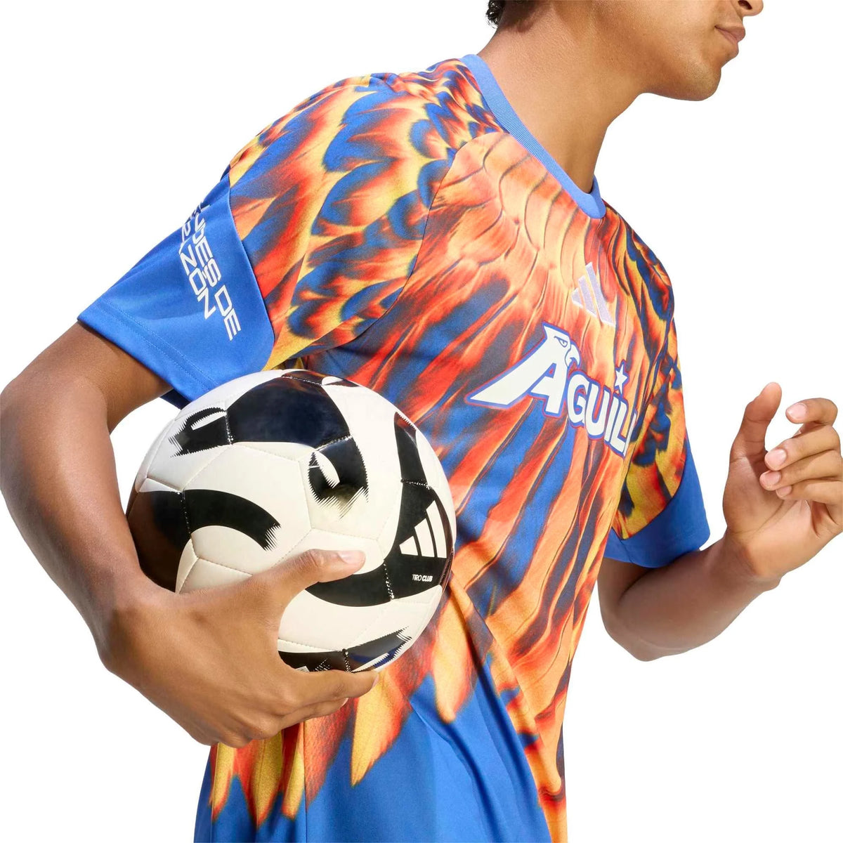 A man wearing a vibrant soccer jersey with a fiery orange, yellow, and blue flame pattern, holding a black and white soccer ball against a solid white background.