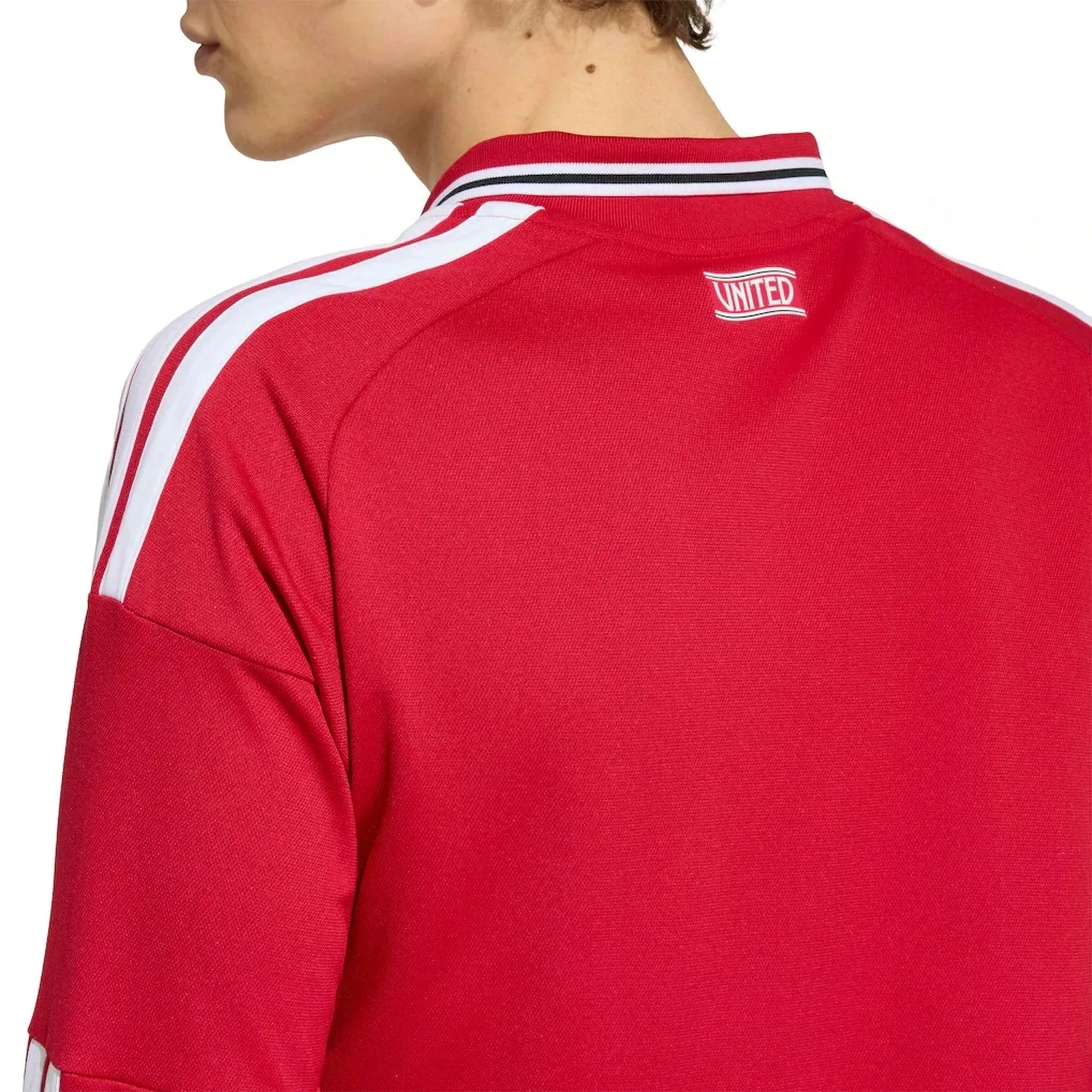 Close-up back view of a person wearing a red long-sleeve sports top with white shoulder stripes, a black and white striped collar, and a small white 'UNITED' logo patch on the upper back.