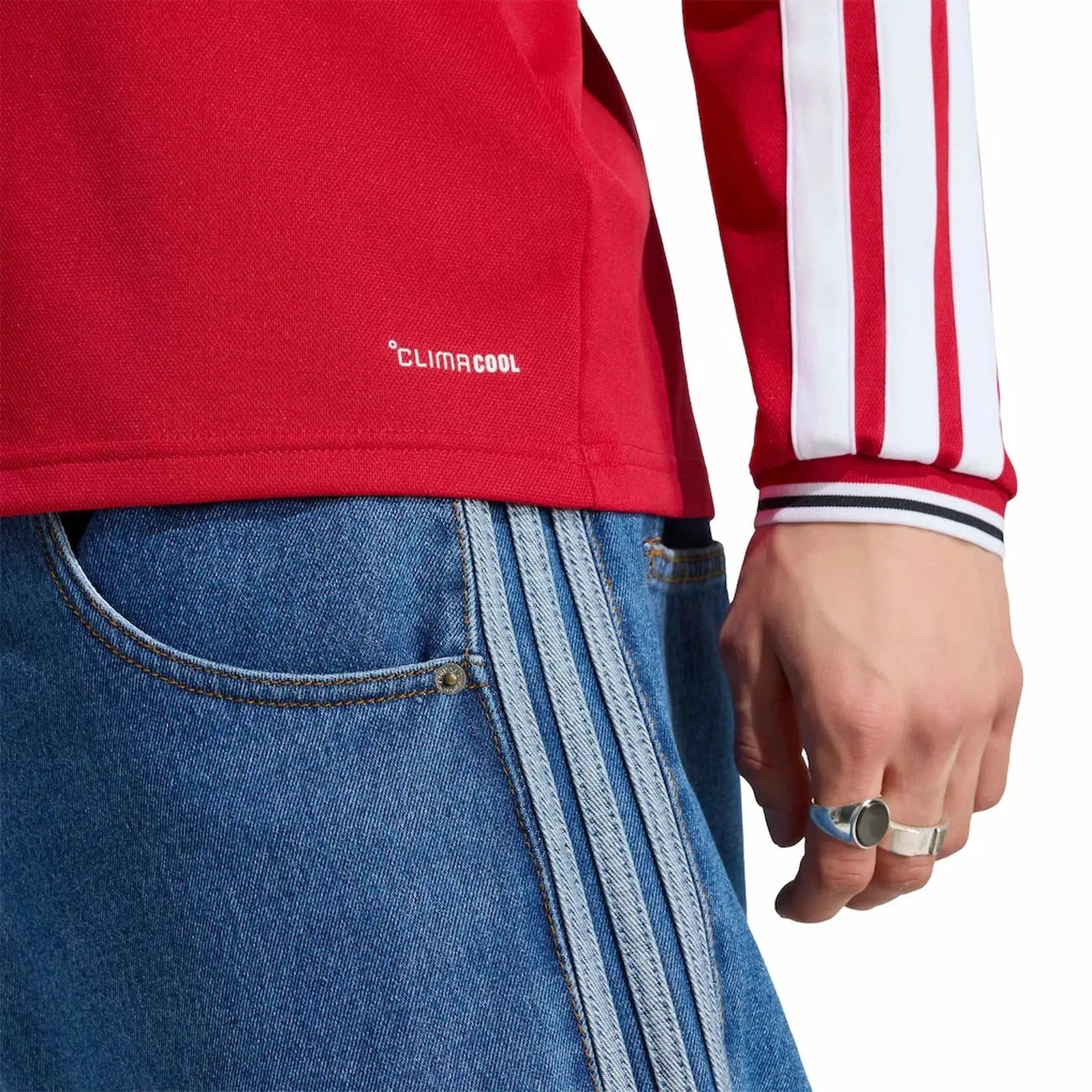 Person wearing a red jacket with 'Climacool' branding, blue jeans with white stripes, and holding a phone.