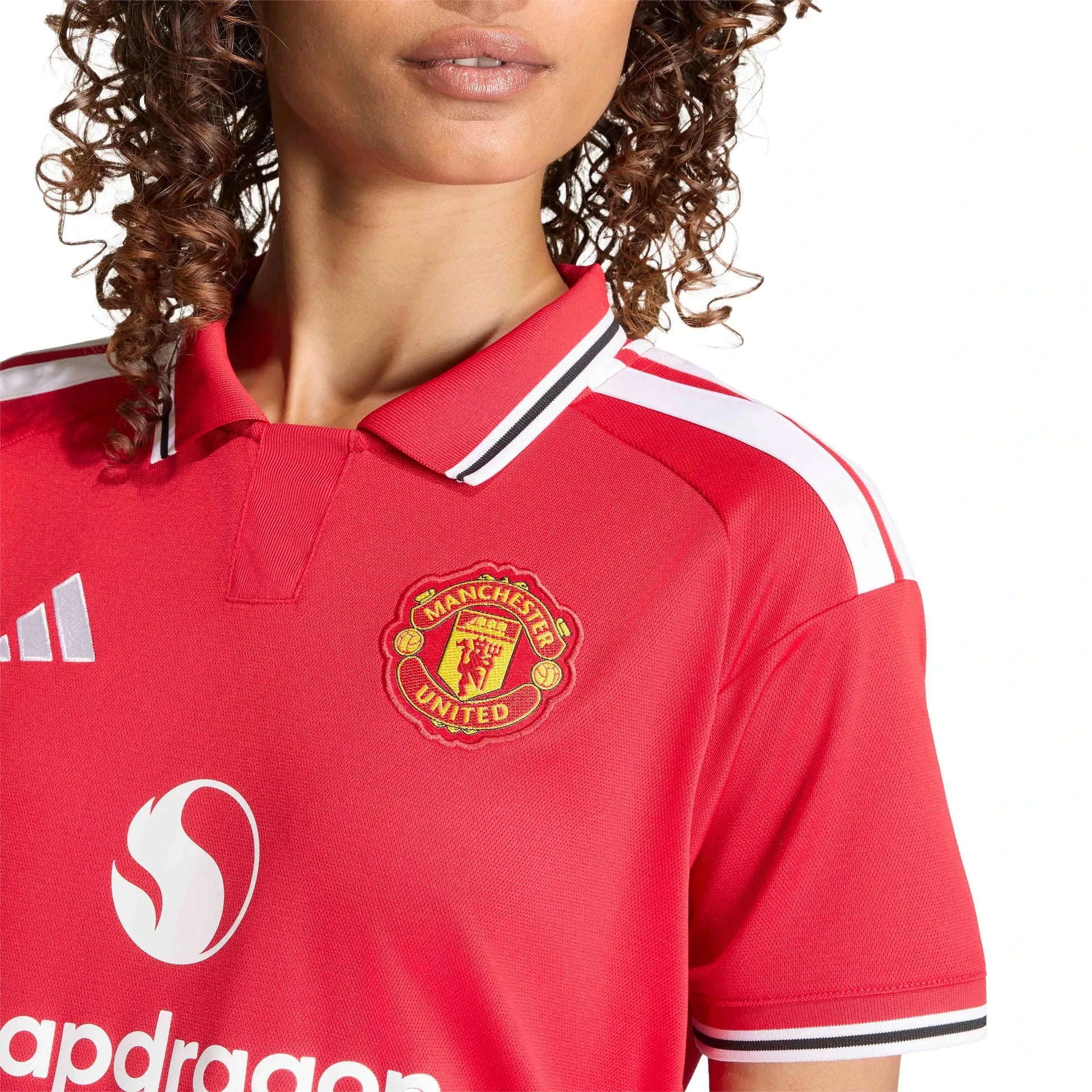 Close-up of a red Manchester United soccer jersey with white and black trim on the collar and sleeves, featuring the Manchester United crest and sponsor logos.