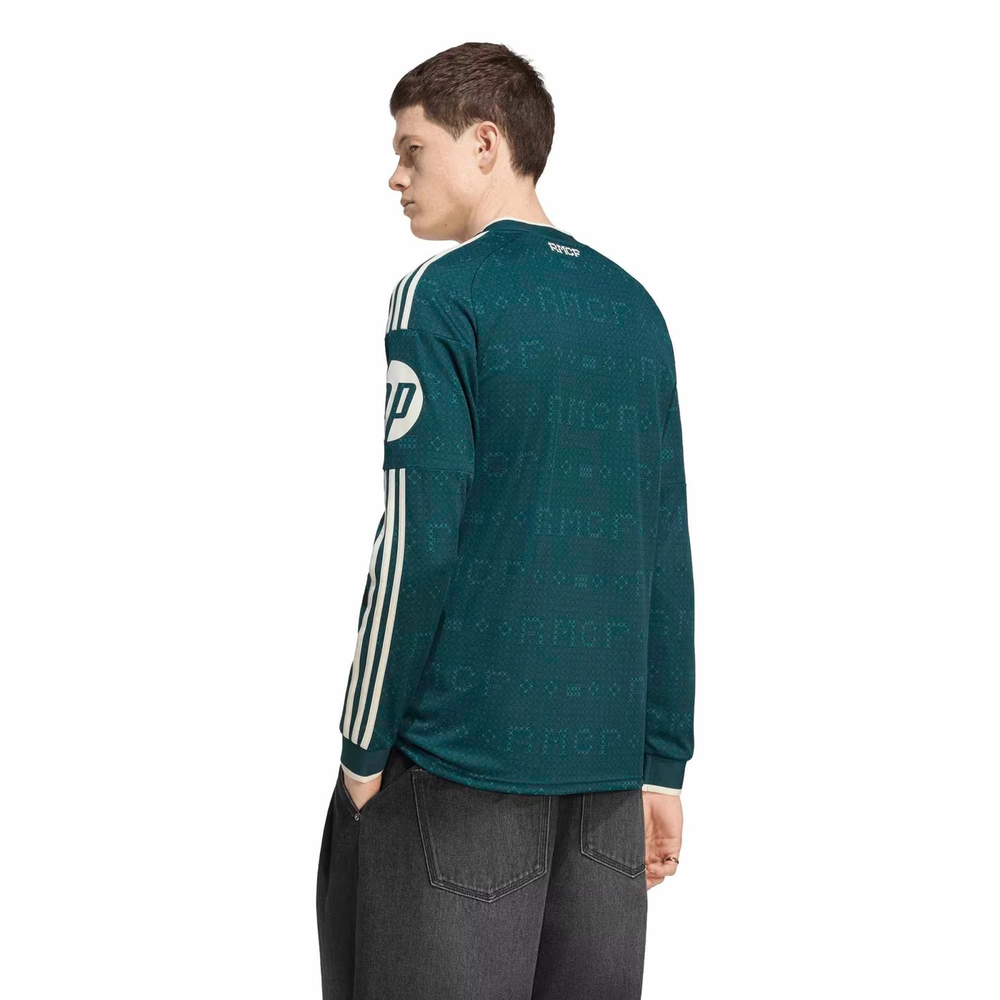 A man wearing a dark teal long-sleeve shirt with white stripes down the sleeves and a white circular logo patch on the upper arm, shown from a three-quarters back view against a plain white background.