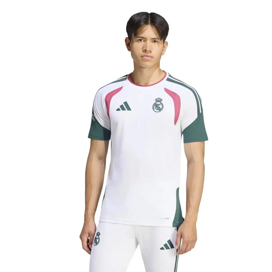 A male model wearing a white Real Madrid soccer jersey with green sleeves and pink accents, paired with matching white shorts, against a plain white background.