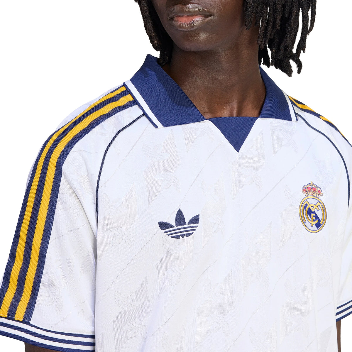 Person wearing a white sports jersey with blue and yellow accents, featuring Adidas and Real Madrid logos.