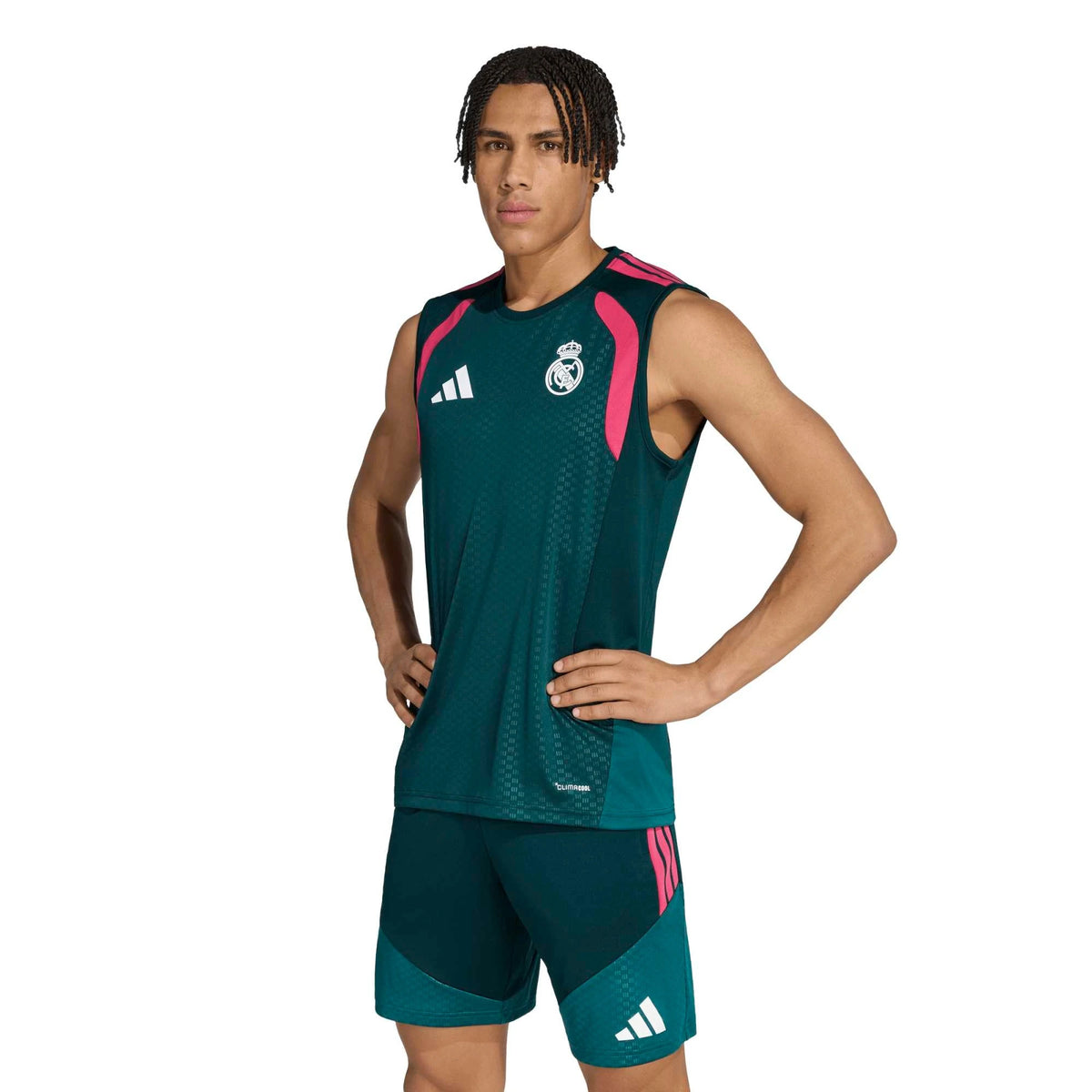 A male model wearing an Adidas Real Madrid training top and shorts set in dark teal green with bright pink accents and white logos, photographed against a solid white background.