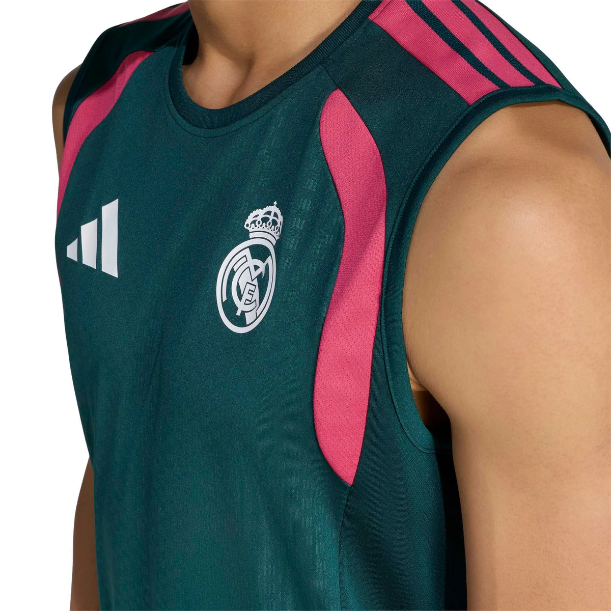 Close-up of a sleeveless Real Madrid training top in dark green with bright pink side panels and white Adidas logo on the chest, worn by a model.