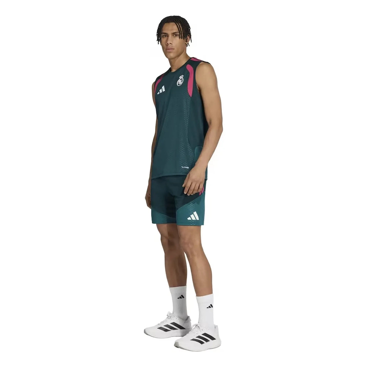 A male model wearing an Adidas athletic training set, featuring a dark teal-green sleeveless top with pink and white accents, matching shorts, white socks, and white Adidas sneakers, set against a plain white background.