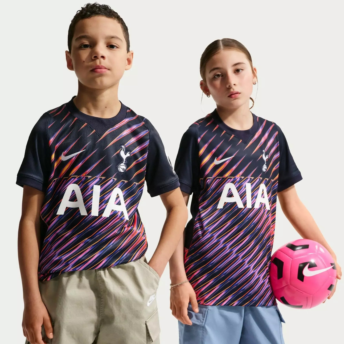 Two children wearing Tottenham Hotspur soccer jerseys with a pink soccer ball.